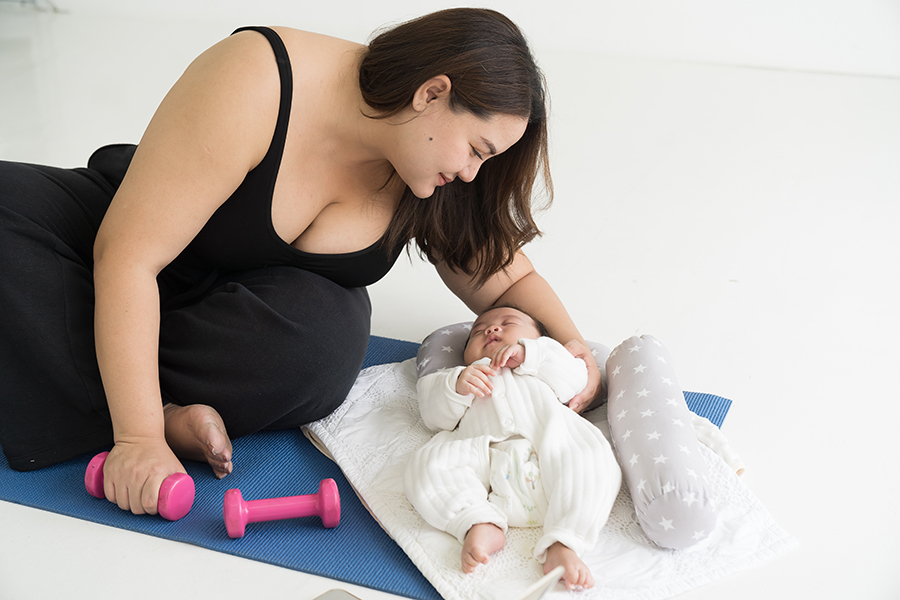 Young mother doing exercises on yoga mat and taking care her newborn at home